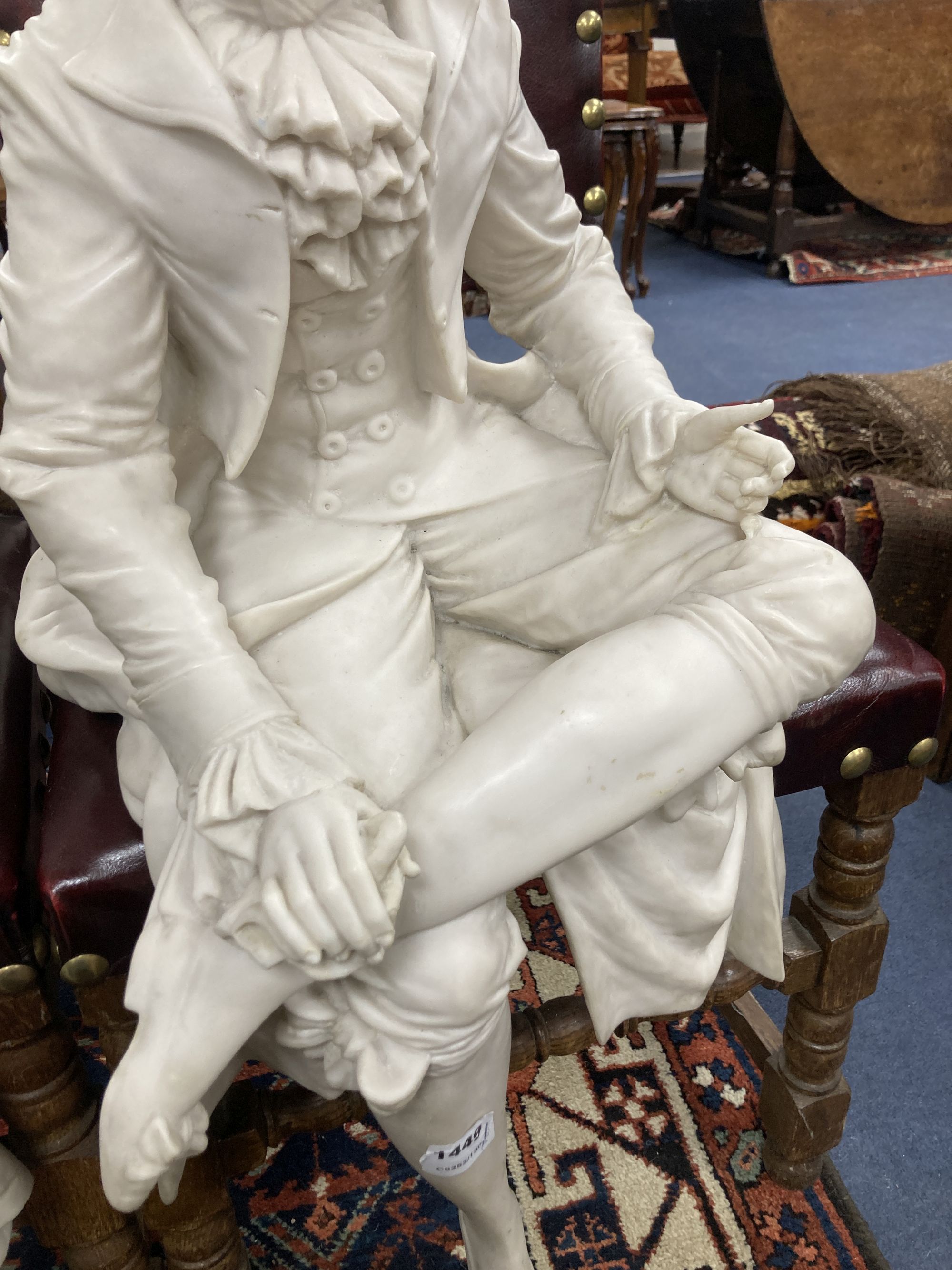 A pair of resin marble seated figures of a Dandy and a Dandizette on ebonised plinths